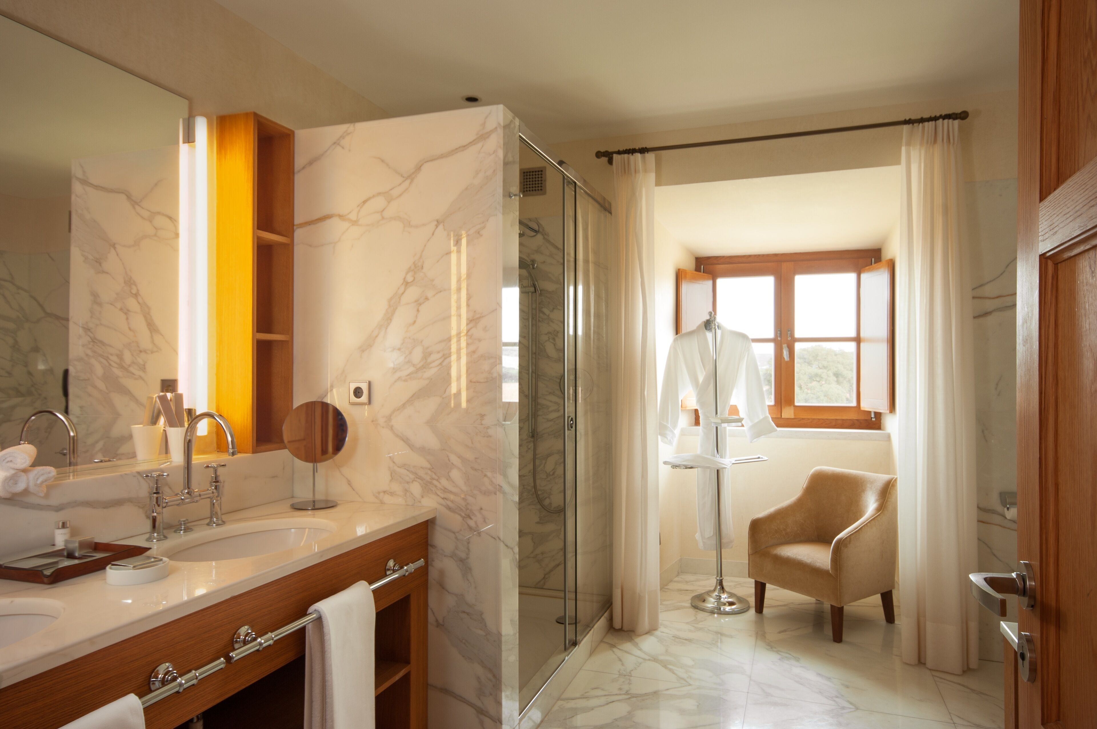 Une salle de bain moderne avec un meuble-lavabo en marbre, une douche à parois de verre et une vue sur un espace extérieur ensoleillé.
