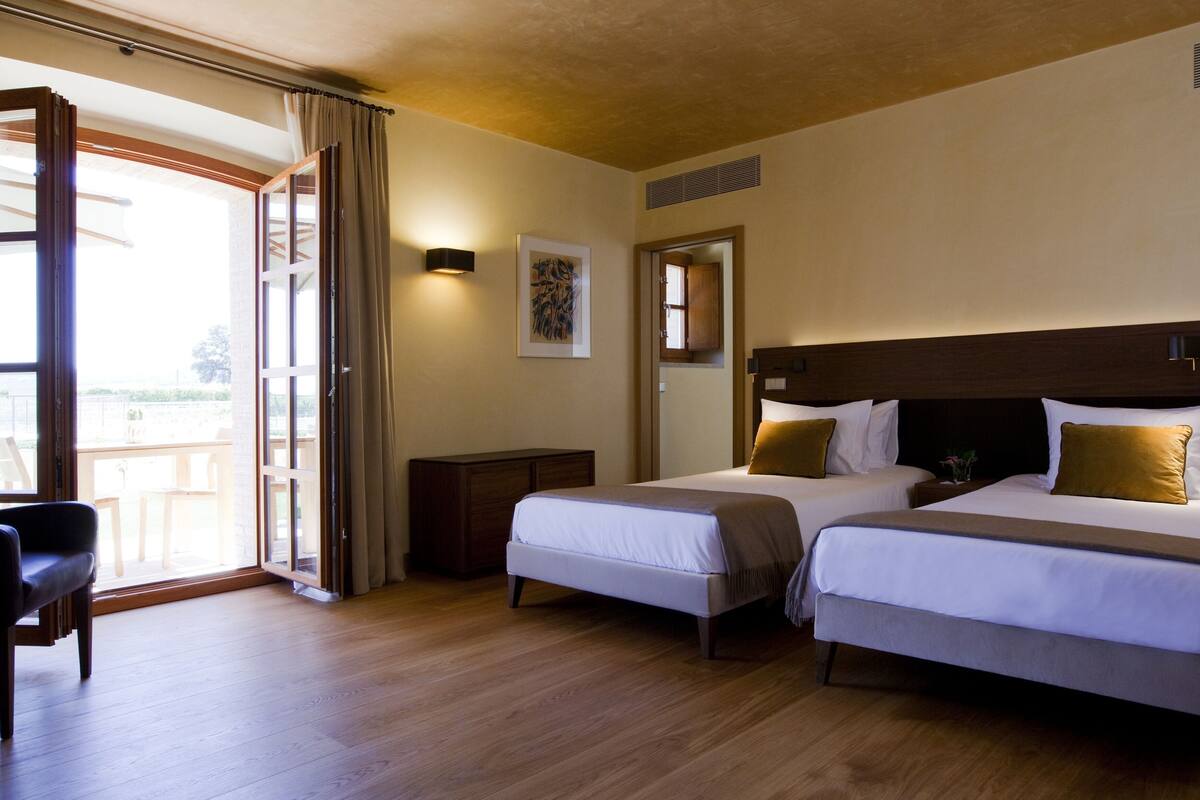 Ein Hotelzimmer mit zwei Betten, einem Schreibtisch und einem großen Fenster mit Vorhängen.