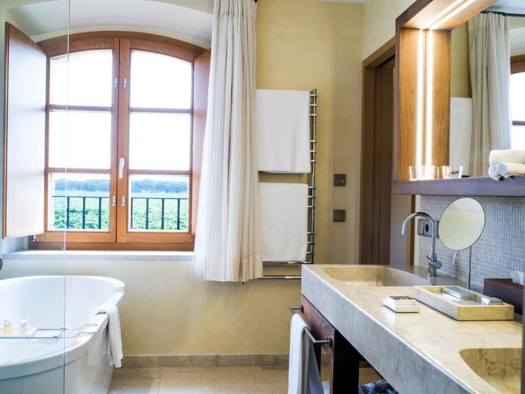 A bathroom with a bathtub, a vanity with a mirror, and a window with curtains.