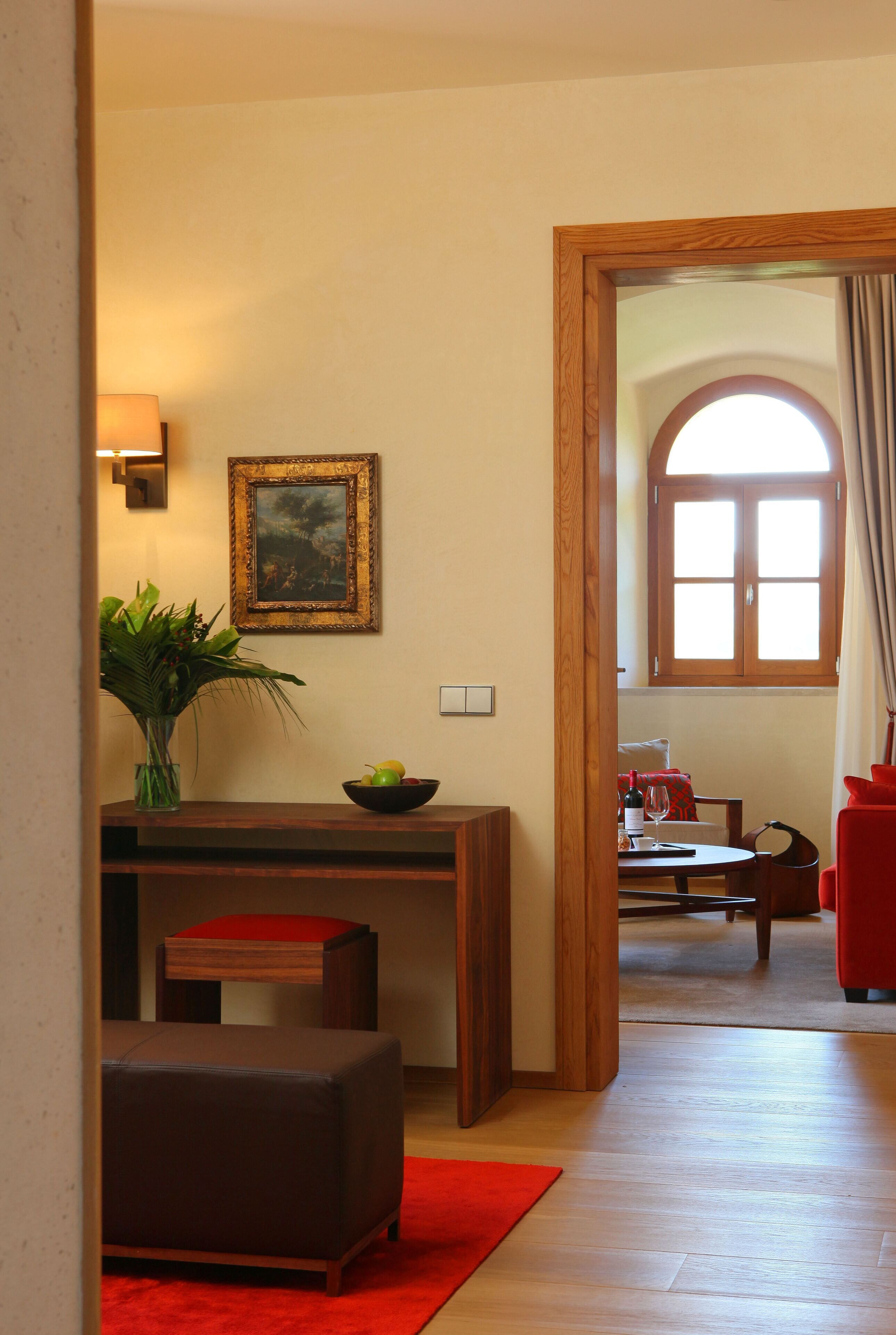 Un salón acogedor con una mesa de madera, un reposapiés rojo, un florero con plantas y un cuadro en la pared.