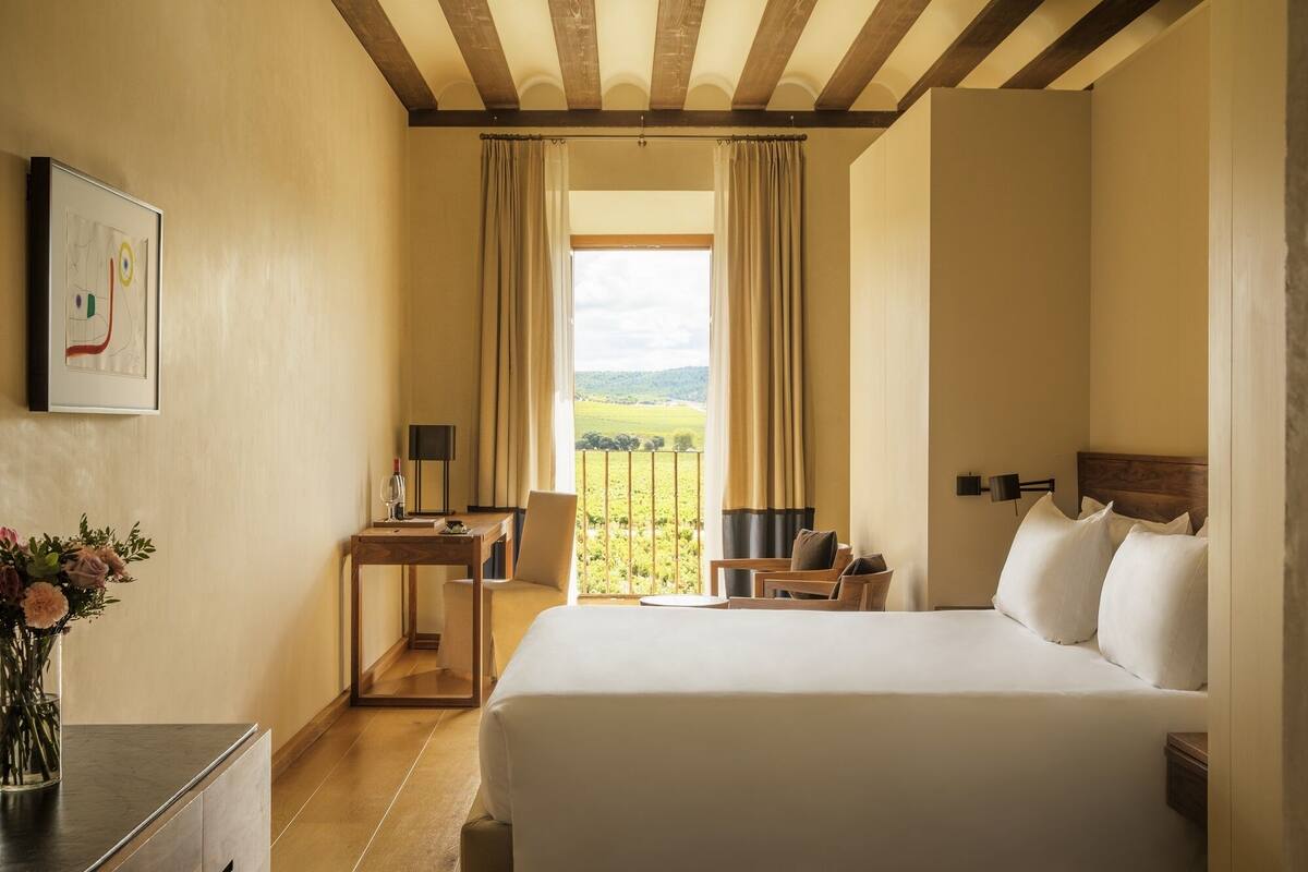 Ein Hotelzimmer mit einem großen Bett, einem Schreibtisch mit Lampe, Blick auf die Landschaft und einem gerahmten Bild an der Wand.
