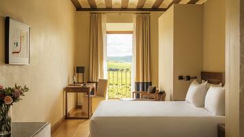 A hotel room with a large bed, a desk with a lamp, a view of the countryside, and a framed picture on the wall.