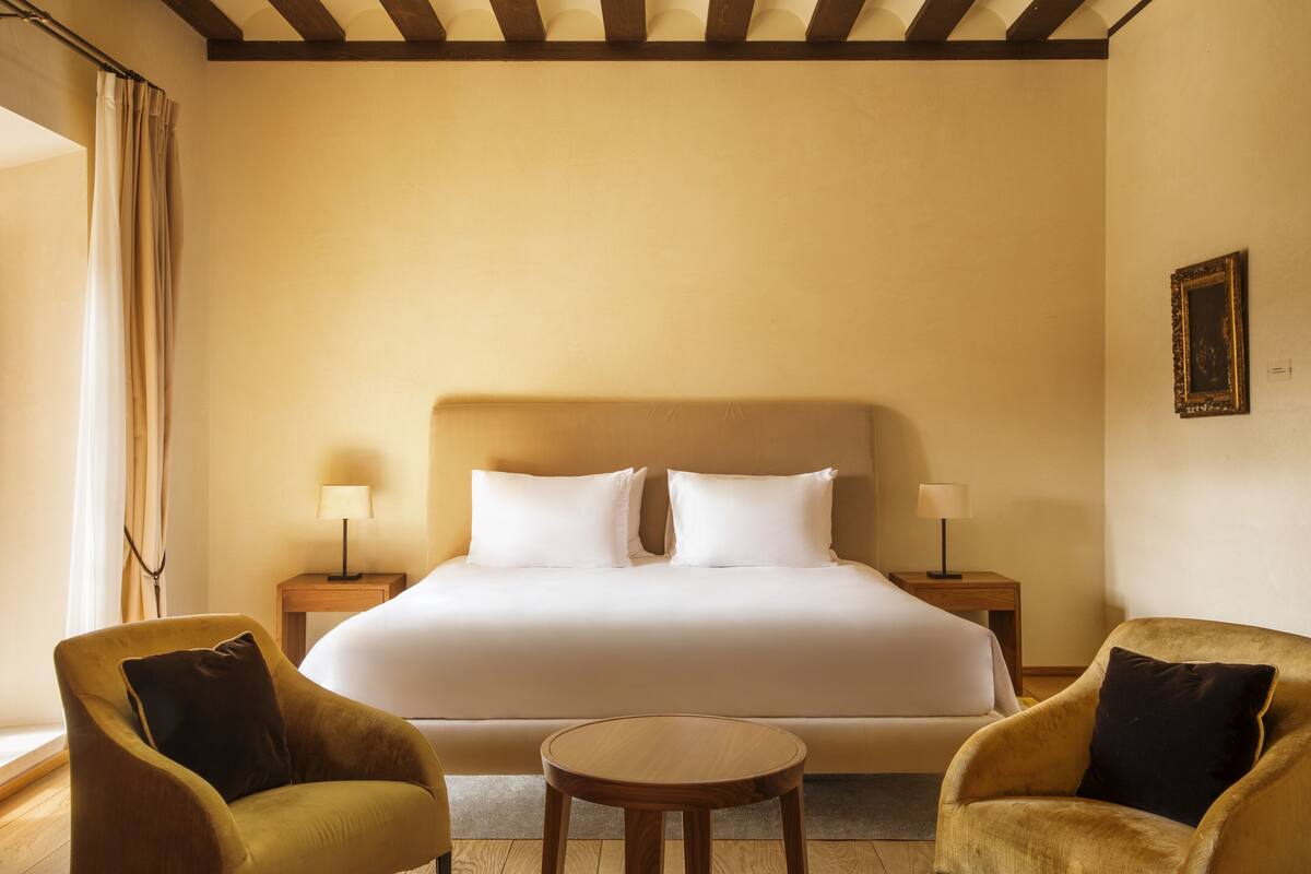 Ein Hotelzimmer mit einem großen Bett, zwei Nachttischen mit Lampen, einem runden Holztisch und zwei Sesseln.
