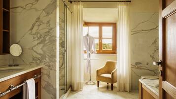 Un baño con pared de mármol, tocador de madera, una silla y una ventana con cortinas.