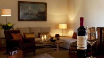 Habitación de hotel con cama, sofá, mesa de centro y una botella de vino con una copa.
