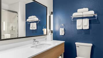 A modern bathroom with a white sink, a large mirror, a blue wall, and a toilet.