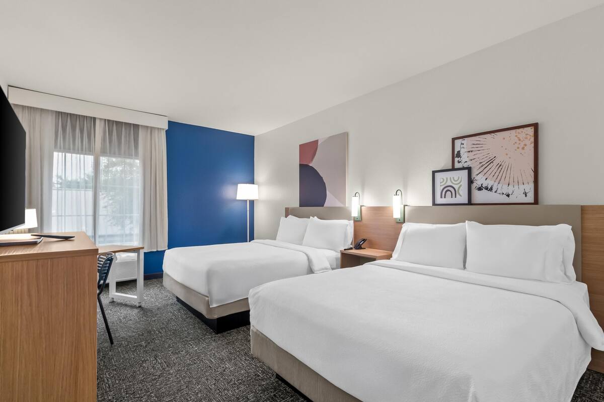 Une chambre d’hôtel avec deux lits, un bureau, une lampe et des œuvres d’art accrochées aux murs.