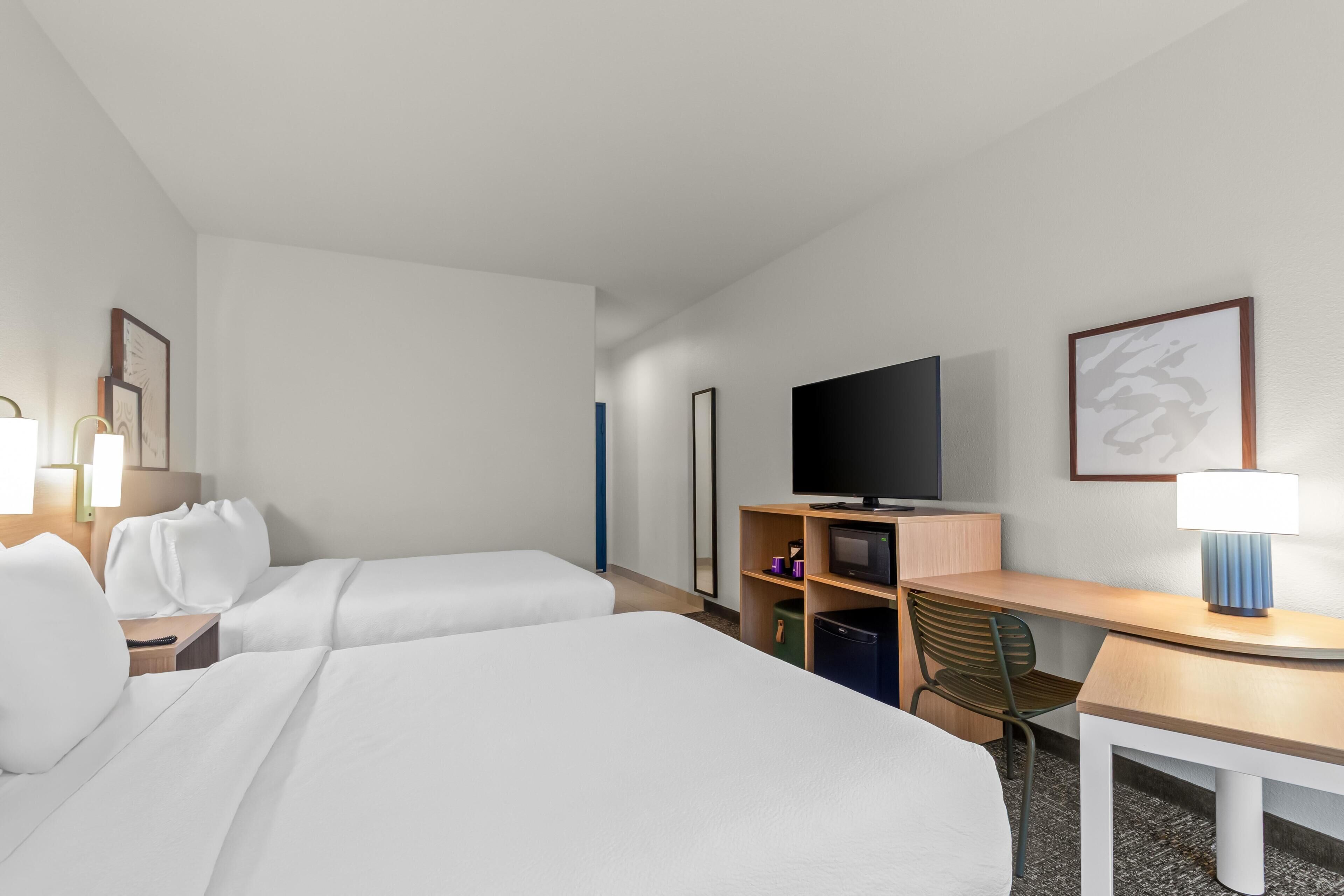 A hotel room with two beds, a desk, a television, and a chair.