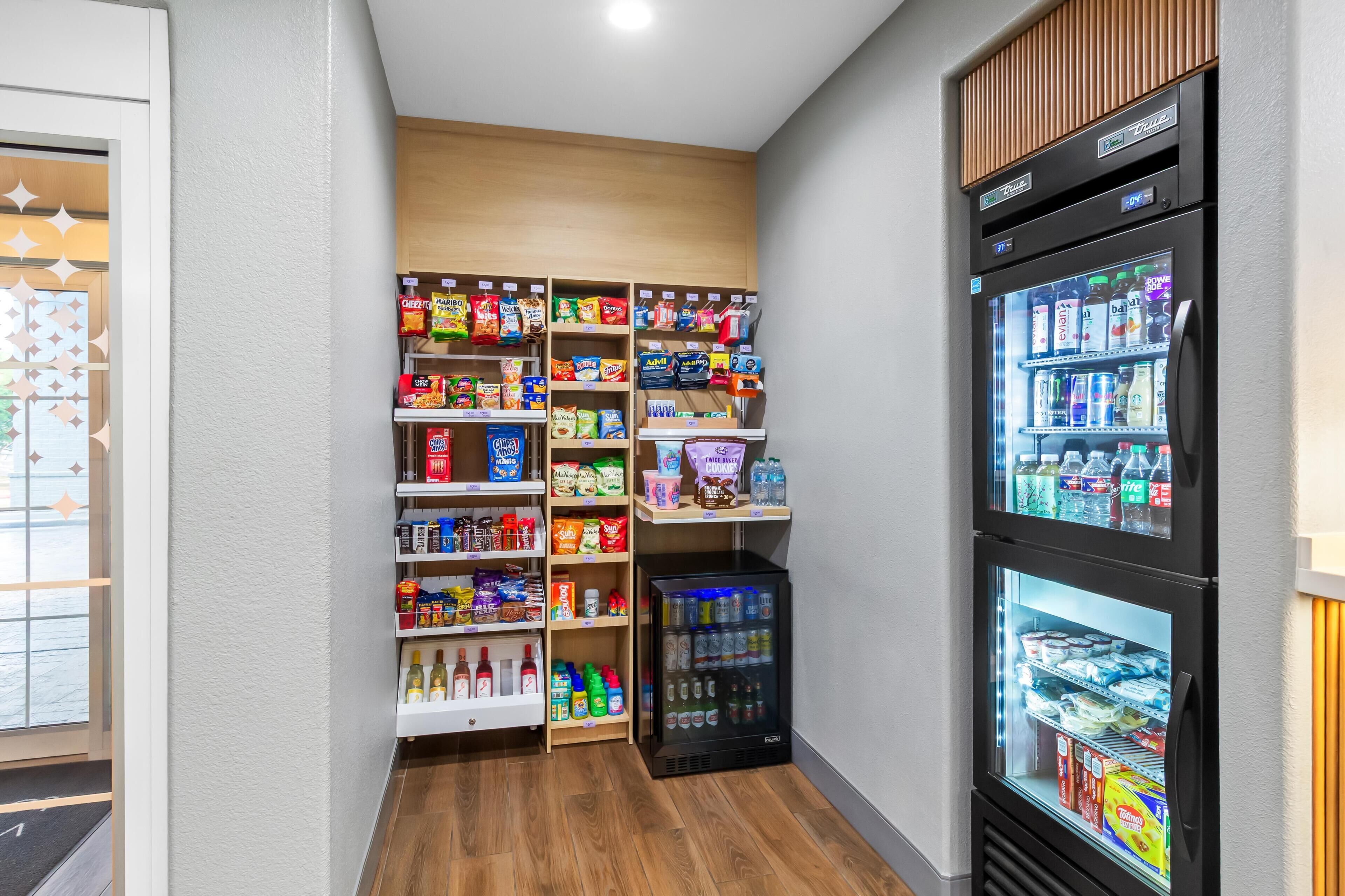 A small, well-organized snack and beverage kiosk with multiple shelves of snacks and drinks, and a refrigerated section.