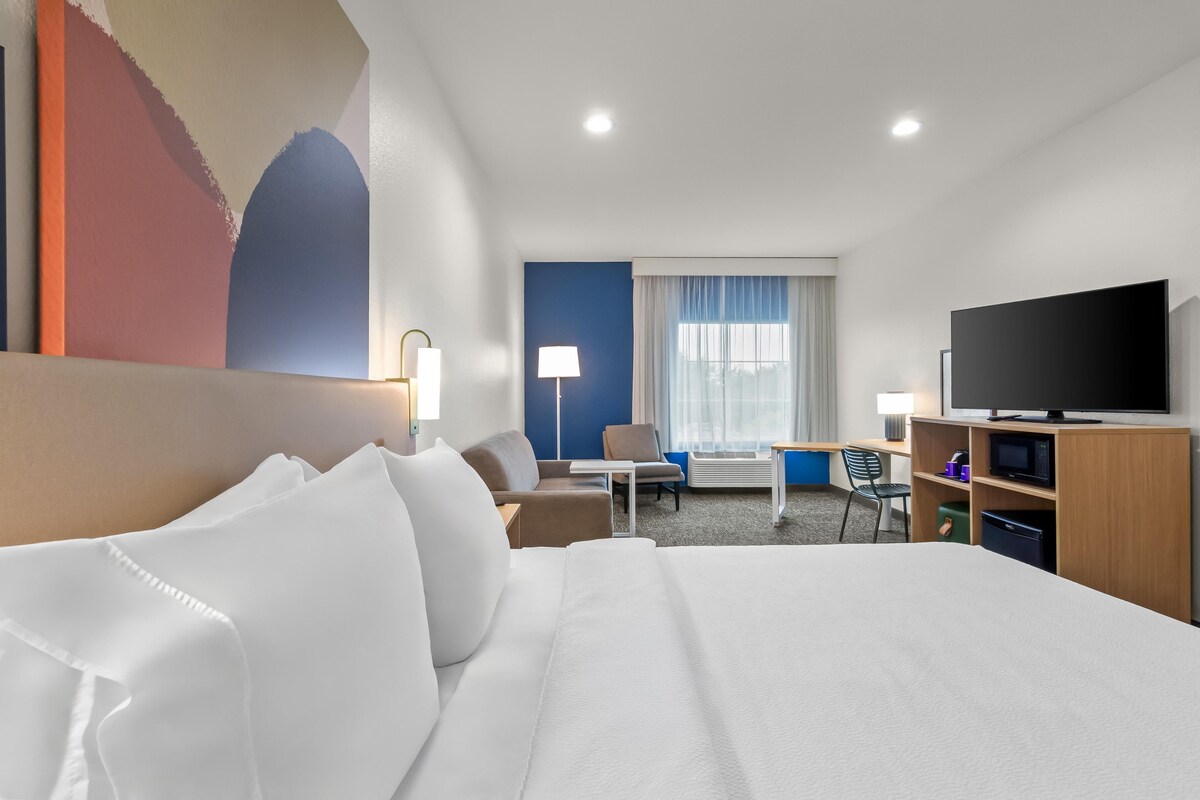 Ein Hotelzimmer mit Bett, Schreibtisch, Stuhl, Fernseher und einem fensterbepflanzten Fenster.