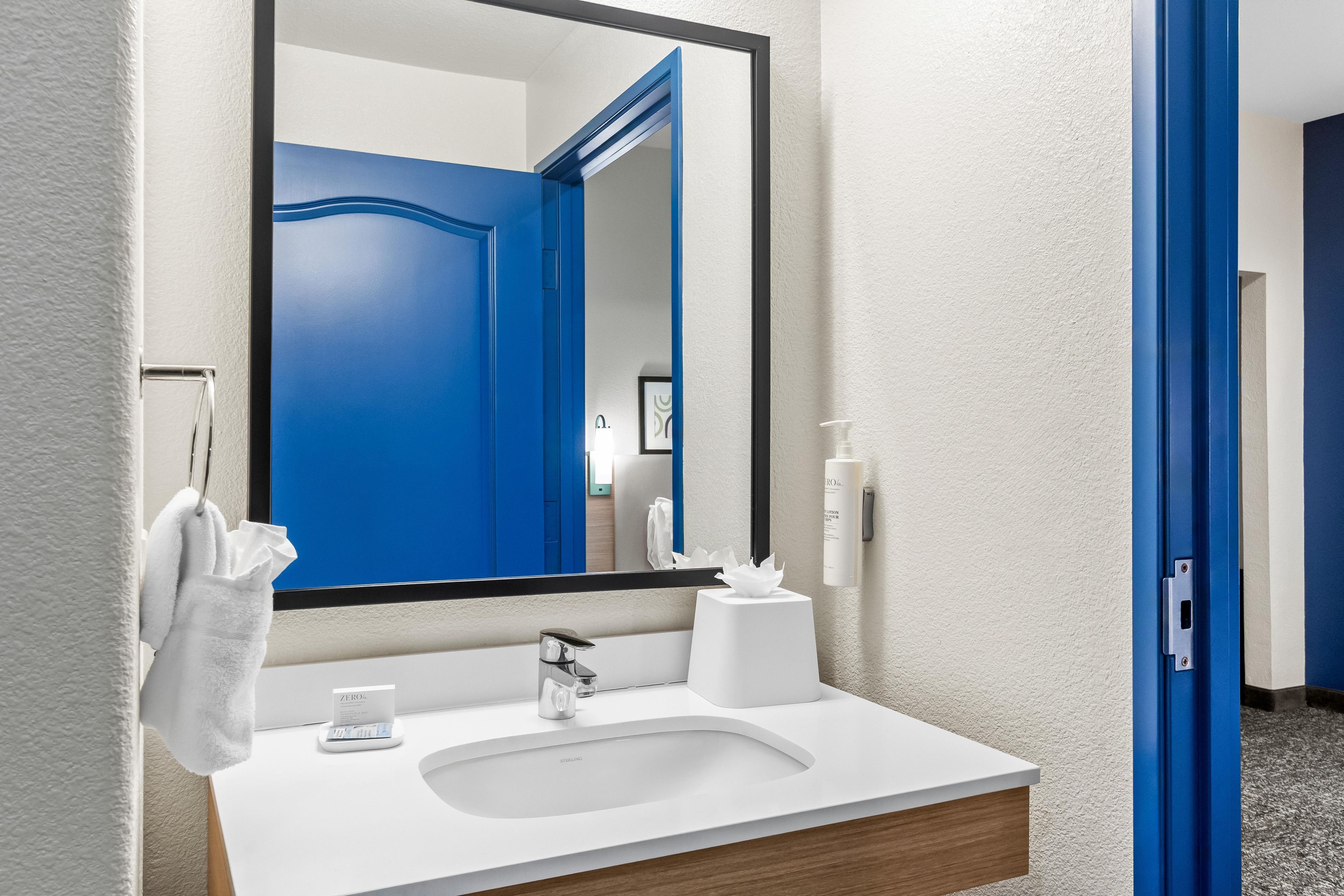 Een badkamer met een wit wastafelmeubel, een grote spiegel, een blauwe deur en een handdoek aan de muur.