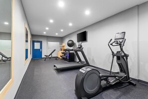 A gym with exercise equipment, a blue door, and a wall-mounted TV. - Spark by Hilton Missouri City Sugar Land (Missouri City)