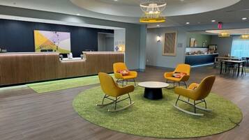 A modern lobby with a reception desk, a circular seating area with yellow chairs, and a green carpet.