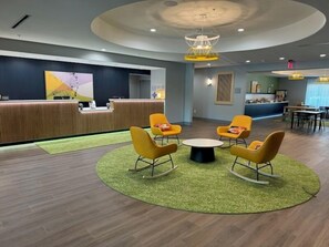Eine moderne Lobby mit einer Rezeption, einer runden Sitzecke mit gelben Stühlen und einem grünen Teppich.