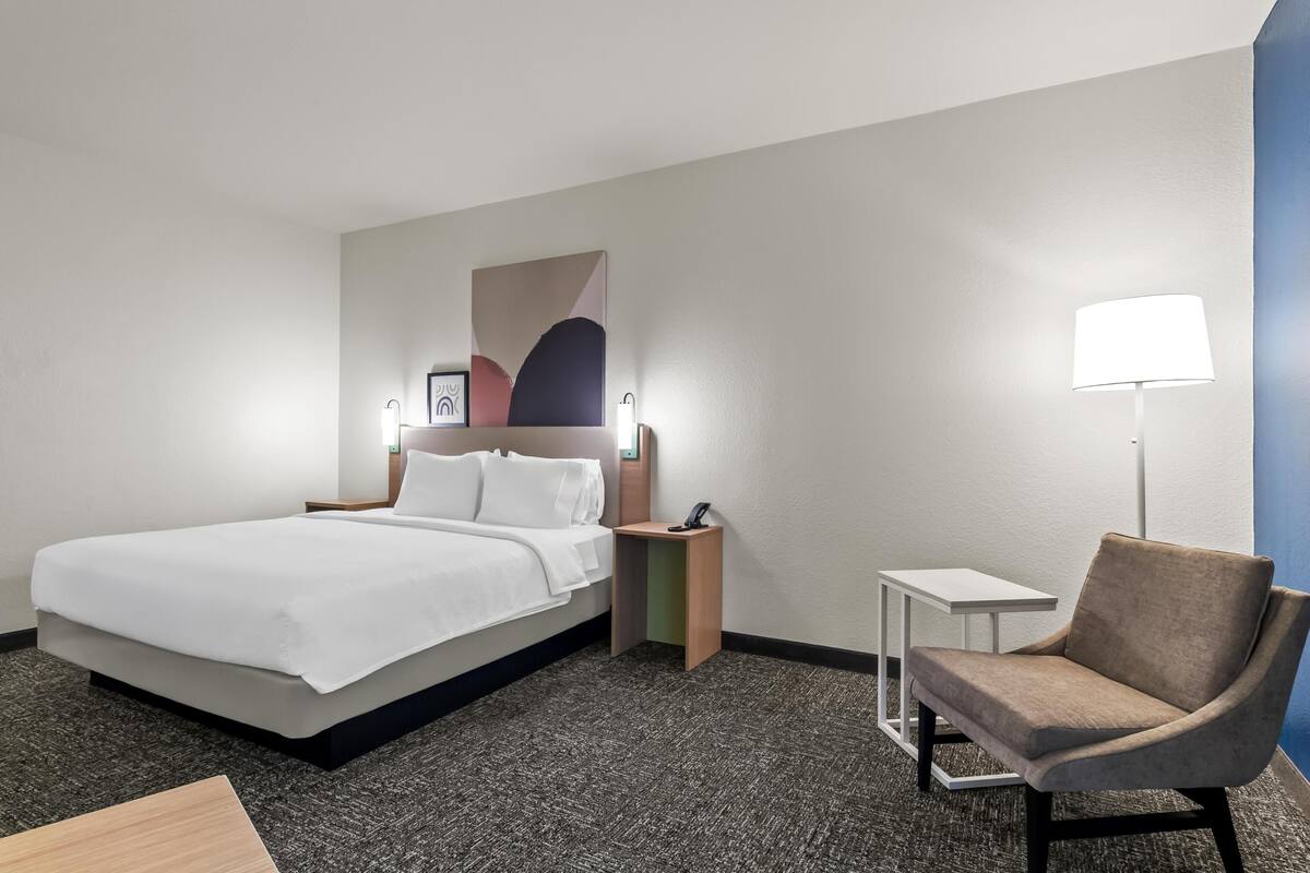 Une chambre d’hôtel avec un lit, une chaise, une table de chevet, une lampe et une petite table.