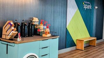 A room with a teal-colored cart with a wheel, a wooden bench, and a wall with a geometric design and the text "Only takes a spark".