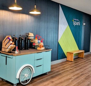 Ein Zimmer mit einem taubenfarbenen Wagen auf Rädern, einer Holzbank und einer Wand mit einem geometrischen Muster sowie dem Text 'Only takes a spark'.