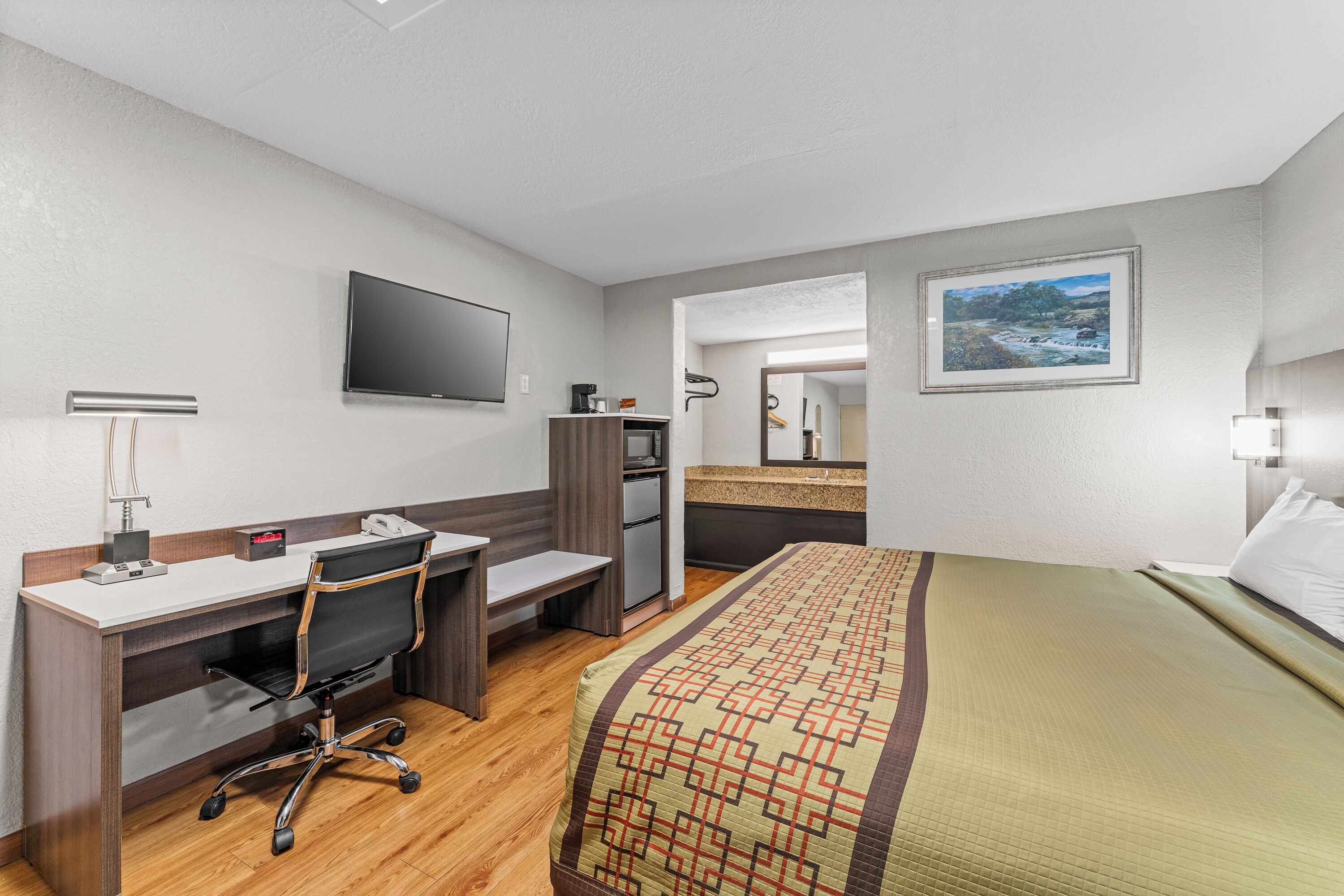 Une chambre d’hôtel avec un lit, un bureau, une chaise, une télévision et un tableau au mur.