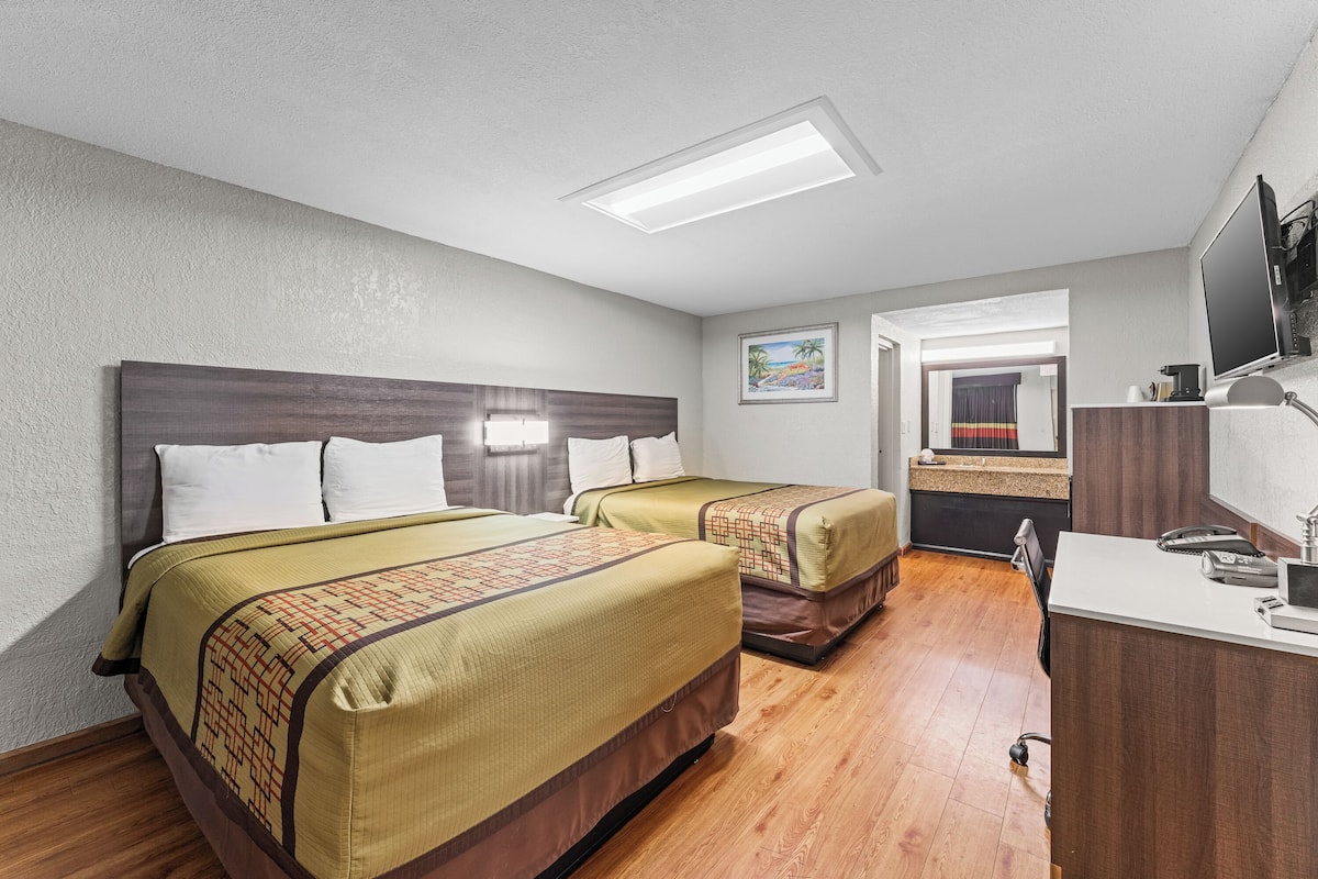A hotel room with two beds, a desk, a television, and a bathroom visible through an open door.