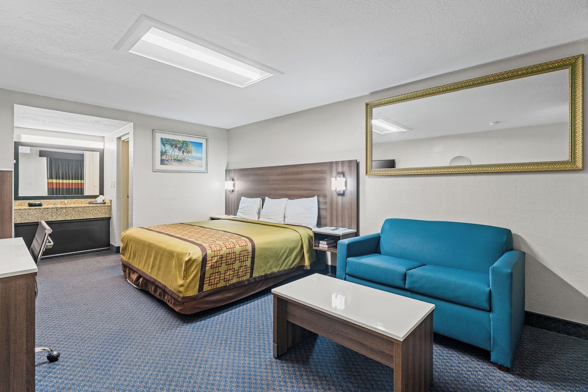 A hotel room with a bed, a blue sofa, a bedside table, a desk, and a large mirror.