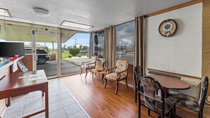A room with a wooden floor, a television, a table, and chairs. There is a window with curtains and a clock on the wall. - Guest Inn (Rogers)