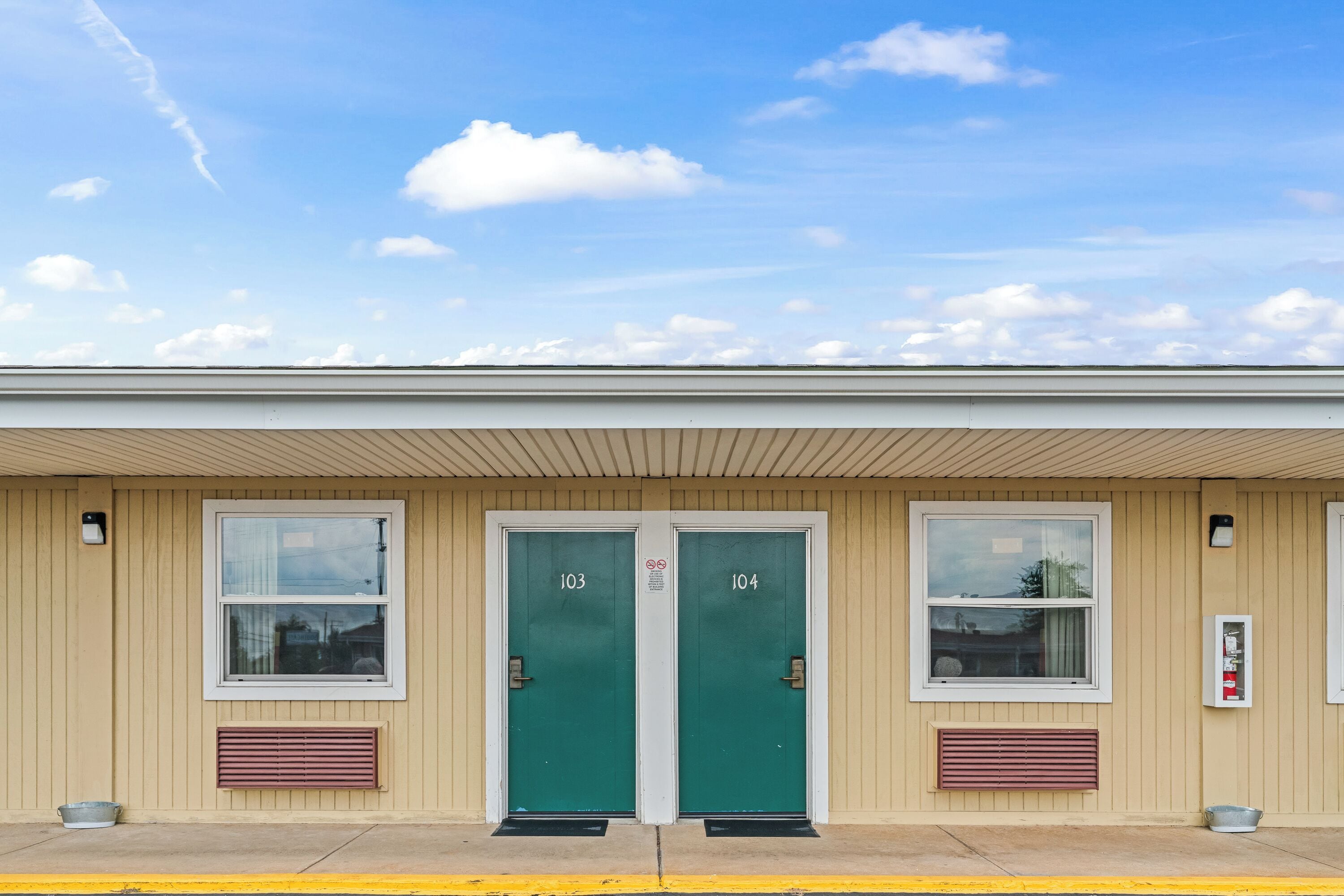 A building with two green doors labeled 103 and 104, a window, and a fire alarm box.