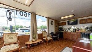 A spacious room with wooden flooring, a large window with curtains, a television mounted on the wall, and a kitchen area with wooden cabinets and a countertop. - Guest Inn (Rogers)