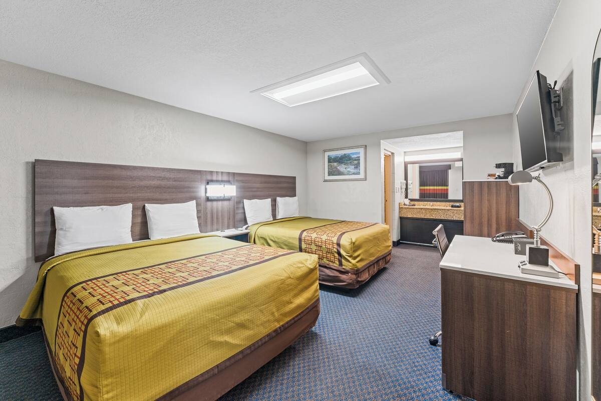 A hotel room with two beds, a desk, a mirror, and a TV.