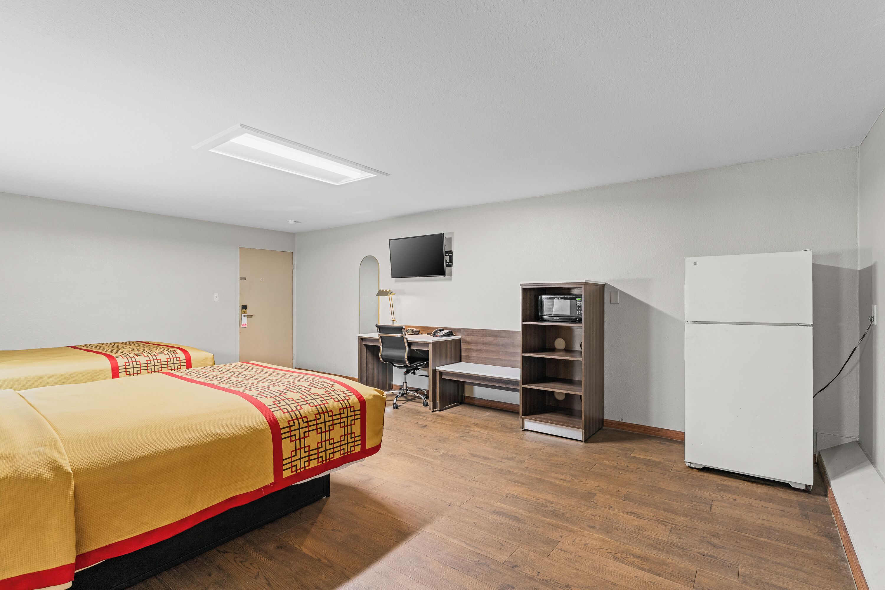 Une chambre d’hôtel avec deux lits, un bureau, une chaise, une télévision et un réfrigérateur.