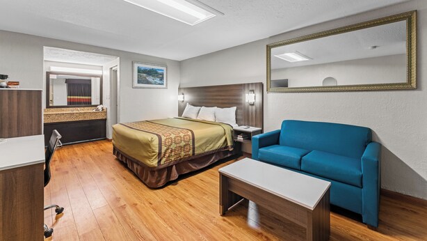 A hotel room with a bed, a blue sofa, a desk, and a mirror. - Guest Inn (Rogers)