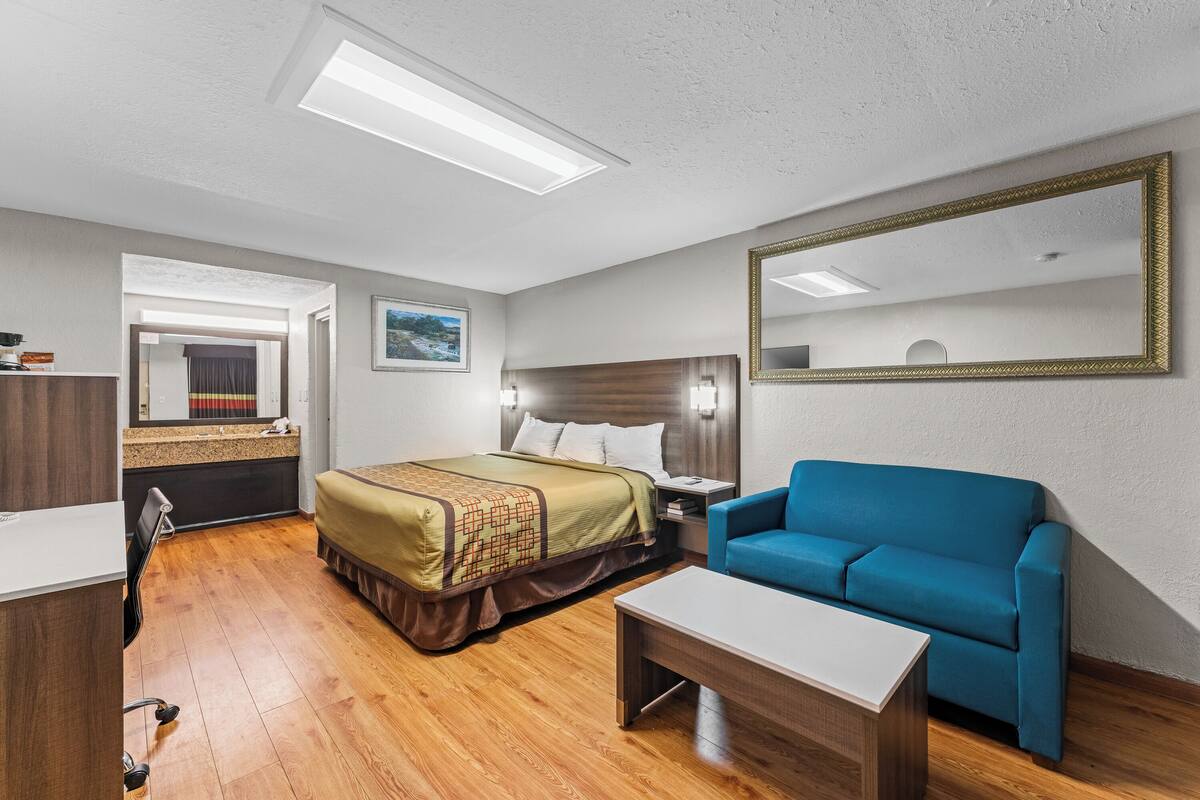 A hotel room with a bed, a blue sofa, a desk, and a mirror.