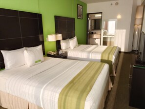 Habitación de hotel con dos camas, una pared de acento verde, un baño con espejo y televisión.