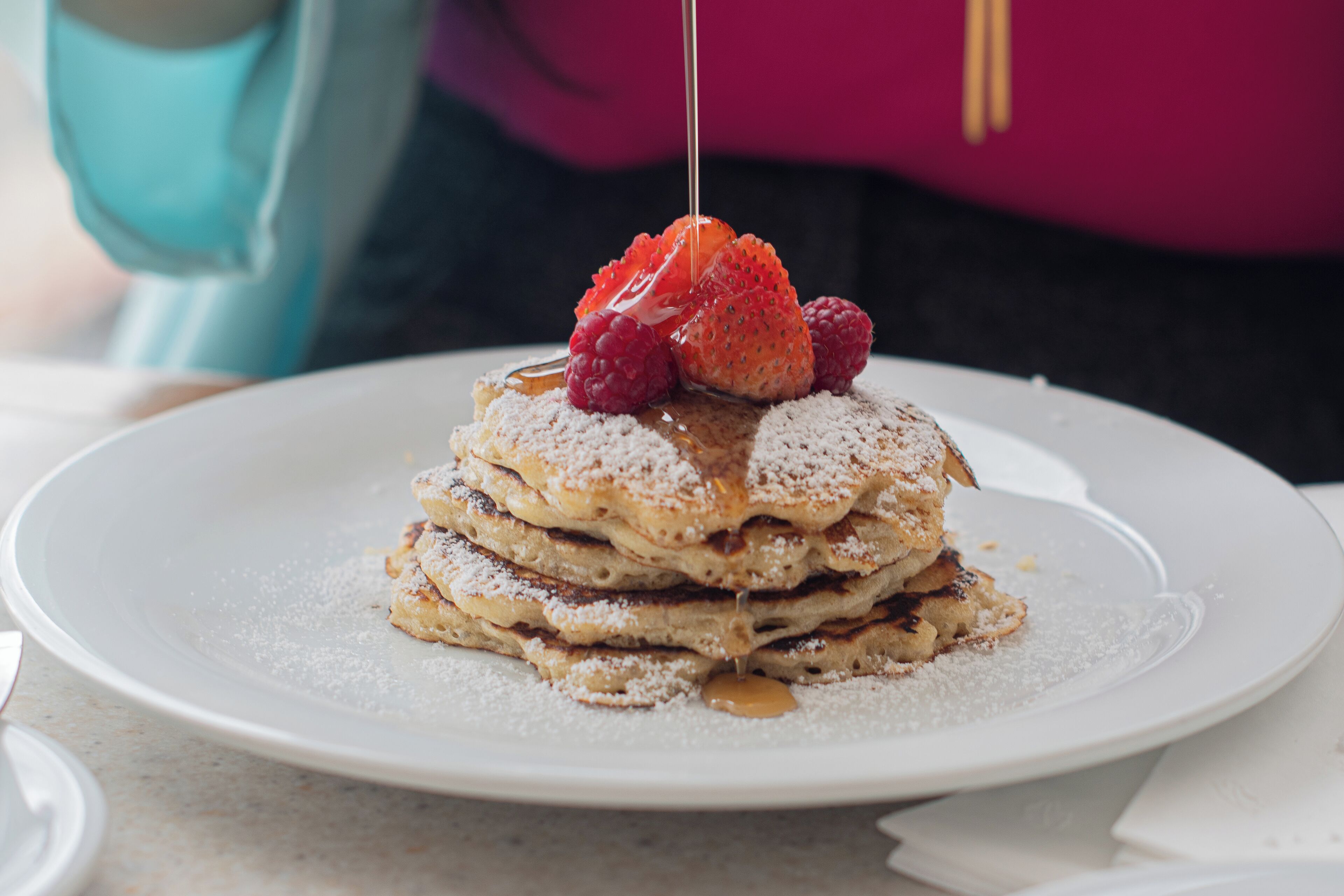 Una pila de tortitas con fresas y frambuesas sobre un plato blanco.