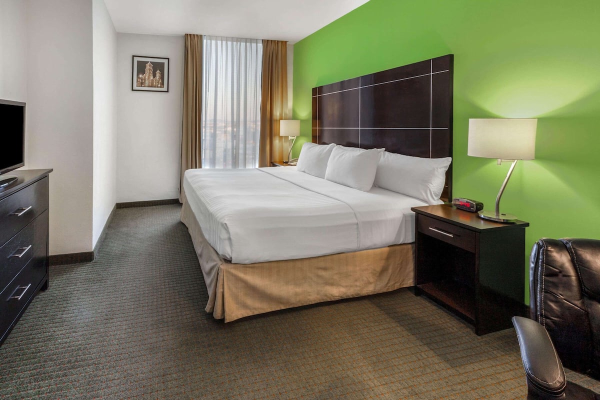 Une chambre d’hôtel avec un grand lit, un bureau, une chaise, une télévision et une fenêtre avec des rideaux.