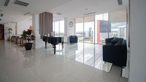 Un hall espacioso con piano, zona de estar y amplias ventanas que ofrecen vistas a la ciudad.