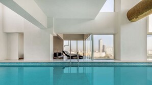 Una piscina interior con agua azul cristalina, un área de descanso con vista a la ciudad y un diseño arquitectónico moderno.