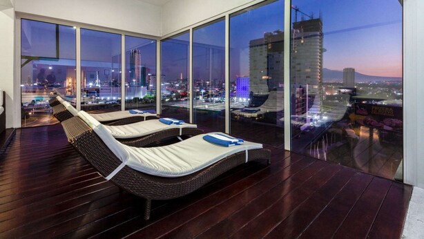 Terraza en la azotea con tumbonas y vistas a la ciudad al anochecer.