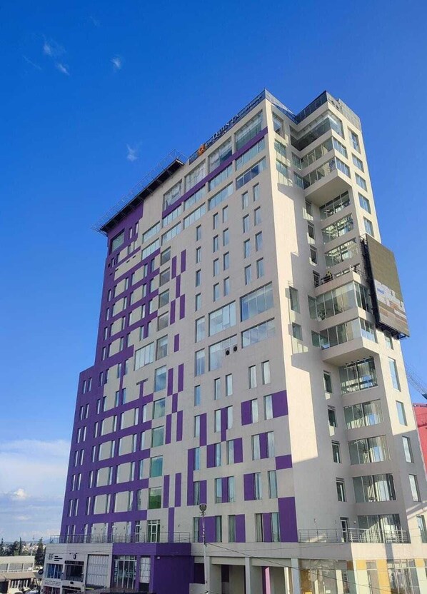 Un hotel de varios pisos con diseño moderno, que combina colores morados y blancos, ventanas amplias y balcones.