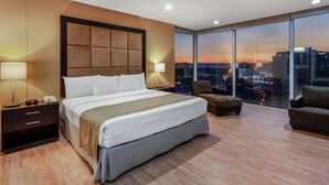 Habitación de hotel moderna con una cama grande, dos mesitas de noche, una silla y un ventanal con vistas a la ciudad.