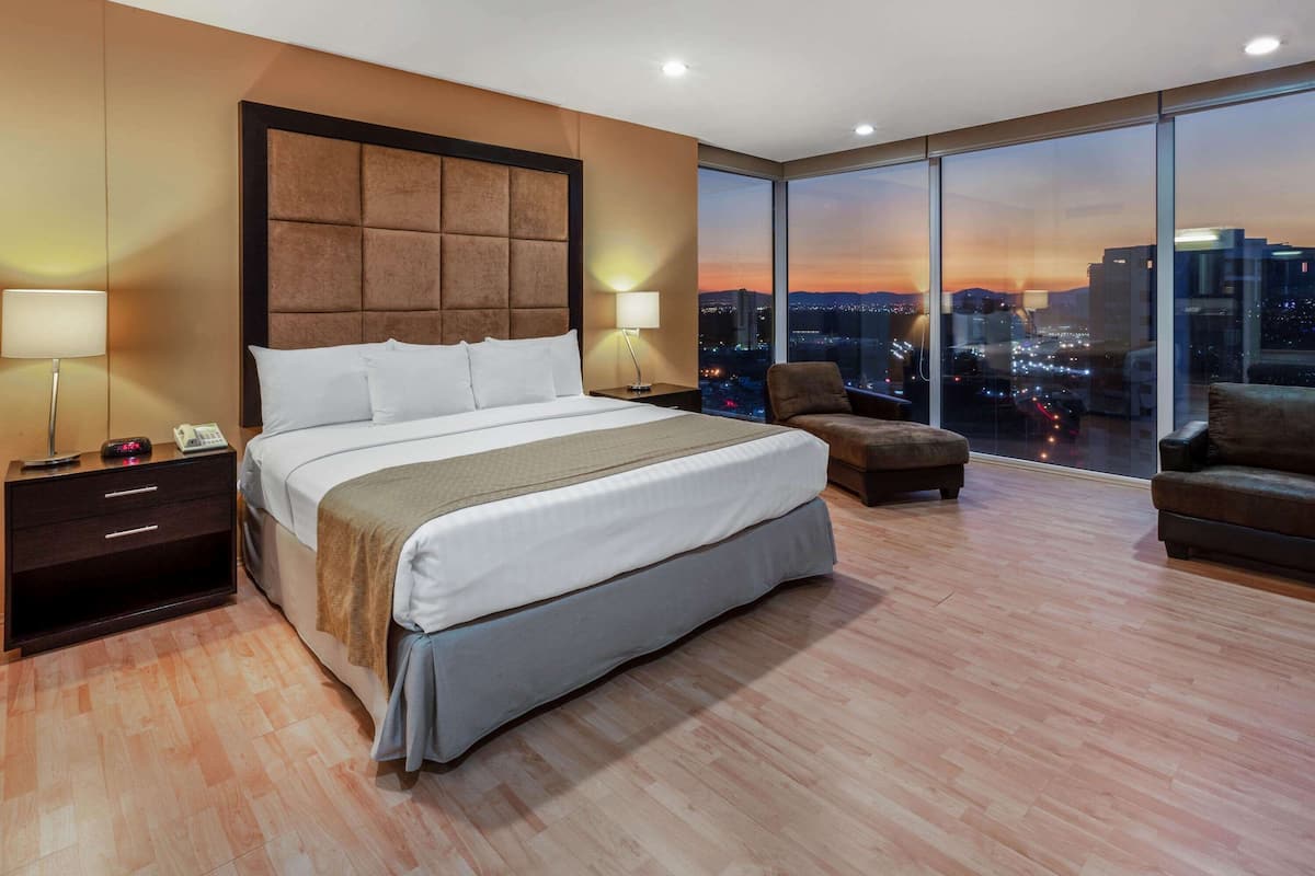 Une chambre d’hôtel moderne dotée d’un grand lit, de deux tables de chevet, d’une petite table, d’une chaise et d’une grande fenêtre donnant sur la ville.