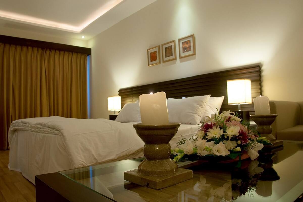A hotel room with a neatly made bed, two bedside lamps, a vase of flowers on a table, and a framed picture on the wall.