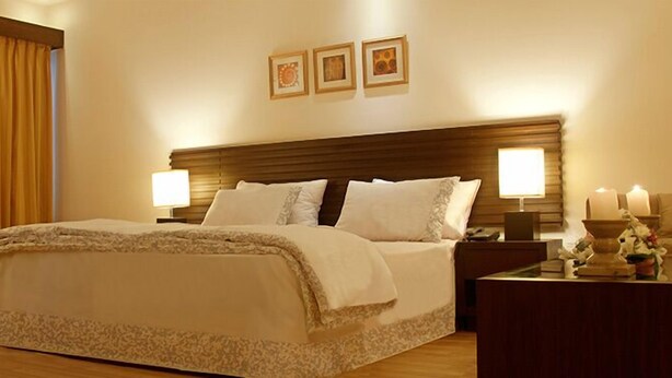 A hotel room with a large bed, two bedside lamps, a nightstand with a lamp, and a wooden headboard.