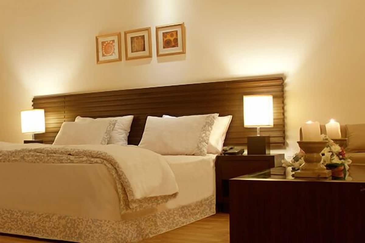 A hotel room with a large bed, two bedside lamps, a nightstand with a lamp, and a wooden headboard.