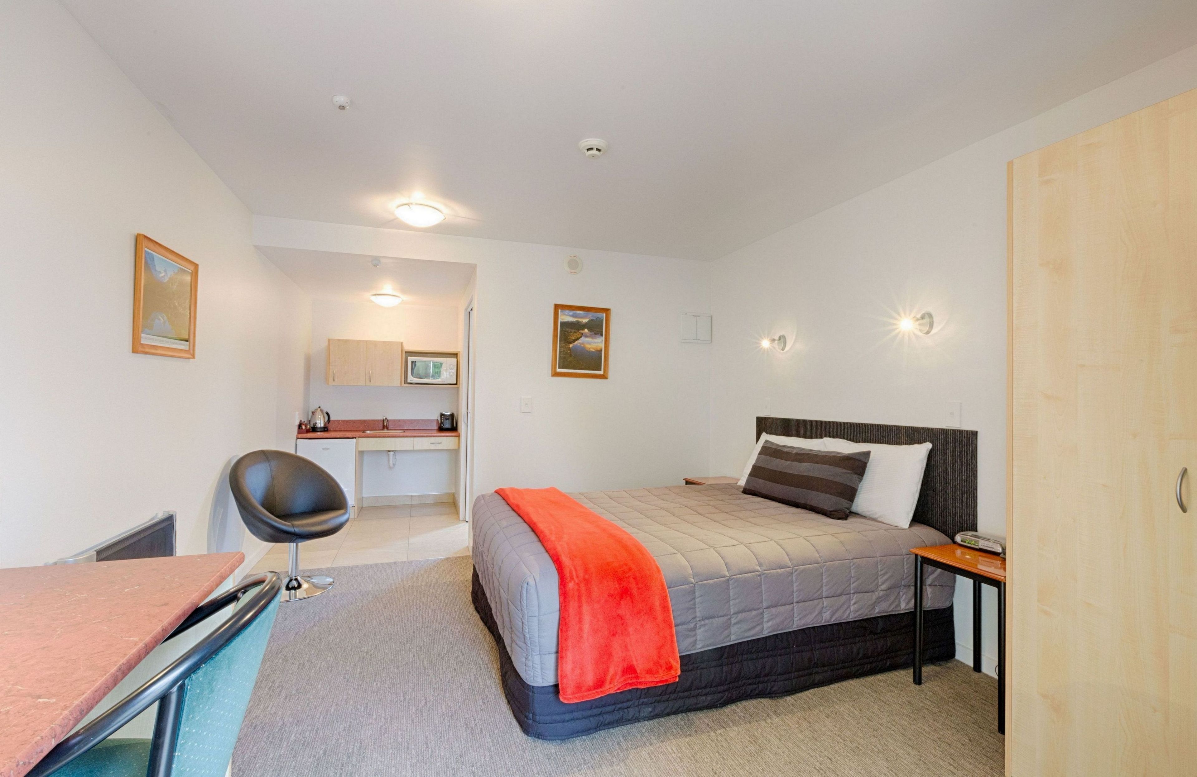 A bedroom with a bed, bedside table, and a desk with a chair.