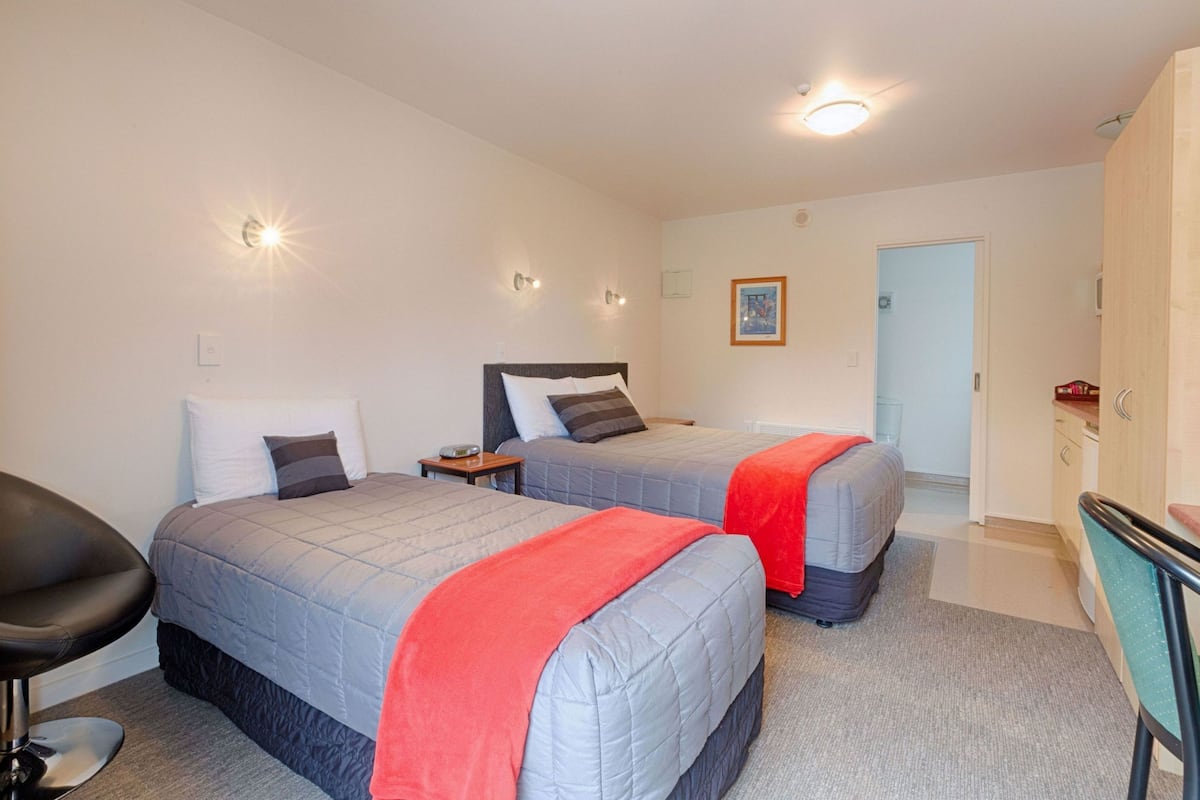Ein Hotelzimmer mit zwei Betten, einem Schreibtisch, einem Stuhl und einer Tür zum Badezimmer.