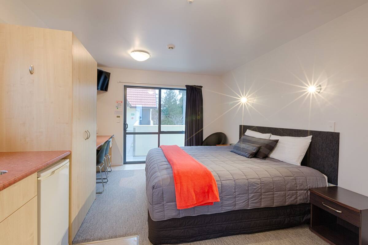Ein Schlafzimmer mit Bett, Nachttisch und Blick ins Freie durch eine Schiebetür.