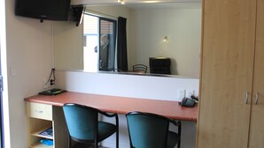 Une pièce comprenant un bureau, deux chaises, un téléviseur fixé au mur, un miroir et une armoire.