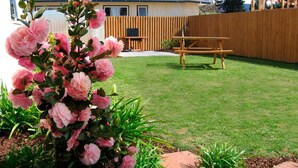 Un jardin avec une table de pique-nique en bois, une clôture en bois et des fleurs roses.