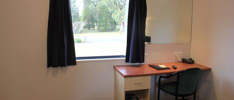 A small room with a desk, chair, and a window with curtains.
