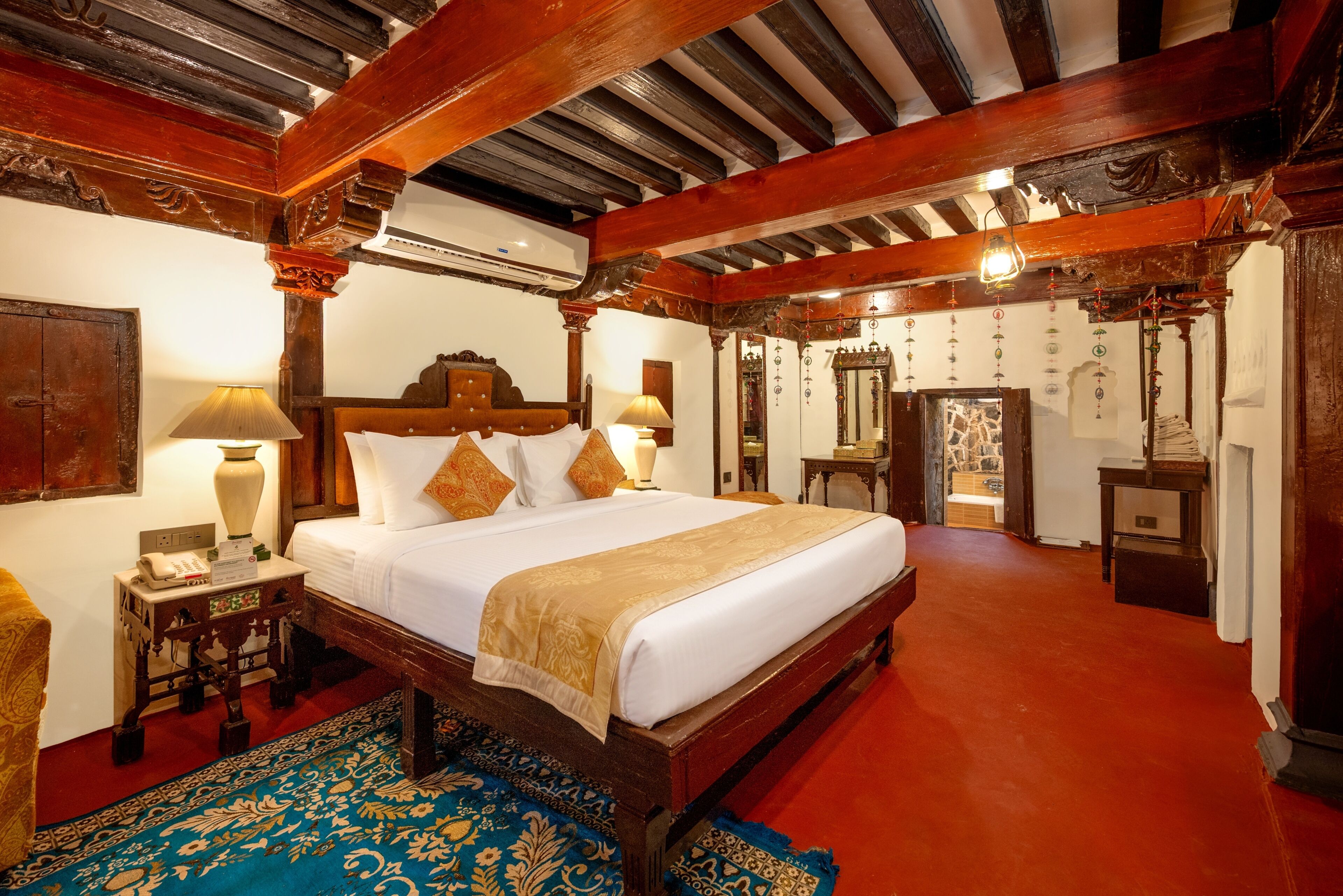 A traditional room with a large bed, wooden beams, a red carpet, and a patterned rug.